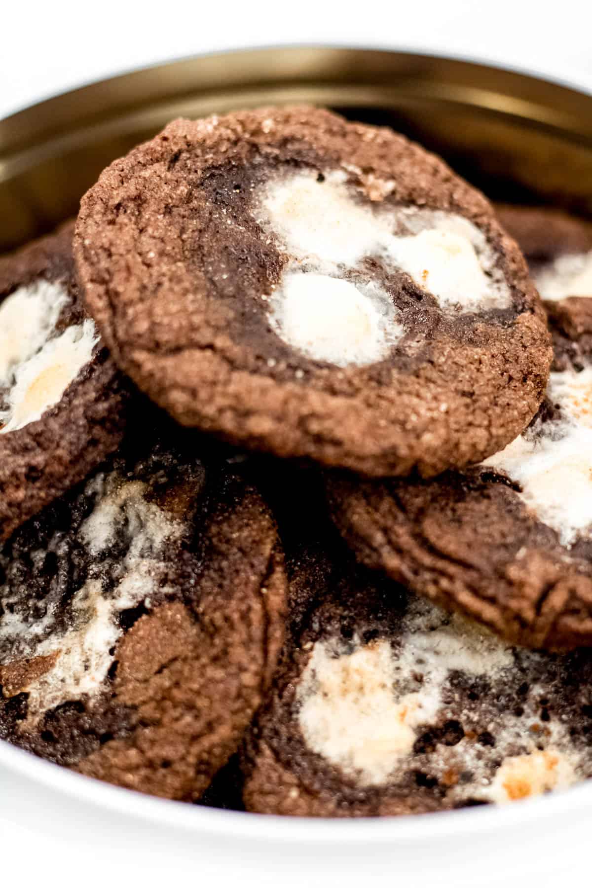 A tin of chocolate cookies with marshmallows on top.