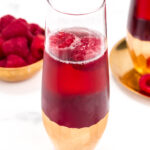 Two glasses with raspberries in them on a marble table.