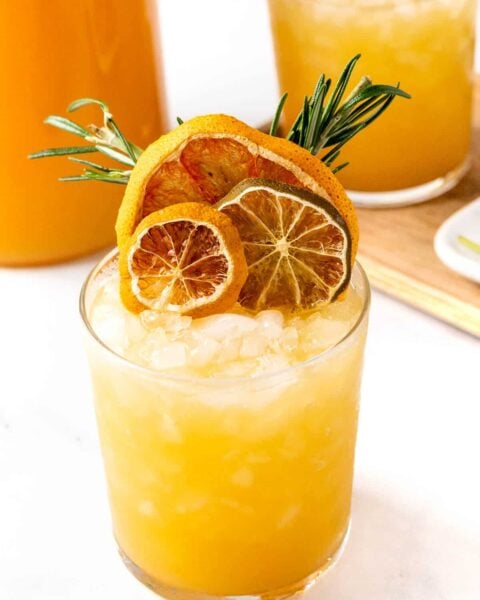 A cocktail with orange slices and rosemary sprigs.