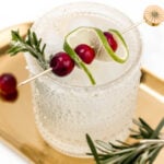 A White Christmas margarita with cranberries and rosemary on a gold tray.