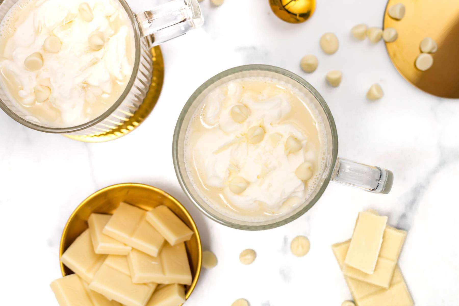 A mug of creamy white hot chocolate topped with whipped cream and white chocolate shavings.