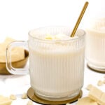 A cup of white hot chocolate with a gold spoon.