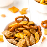 A bowl of chex mix on a wooden table.