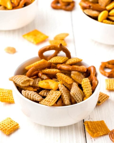 Chex mix in white bowls on a wooden table.
