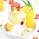 A tray of fruity drinks with limes, strawberries, and pineapples.