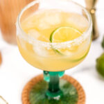 A Virgin Margarita in a glass with lime and lime wedges.