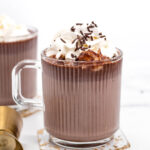 Two mugs of hot chocolate with whipped cream on top.