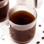 Two cups of coffee with coffee beans in them.