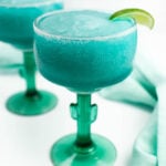 Two glasses of blue margarita with limes on a napkin.