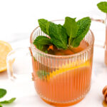 A cup of tea with mint leaves and lemons.