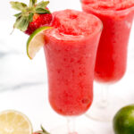 Two glasses of strawberry smoothie with limes and strawberries.