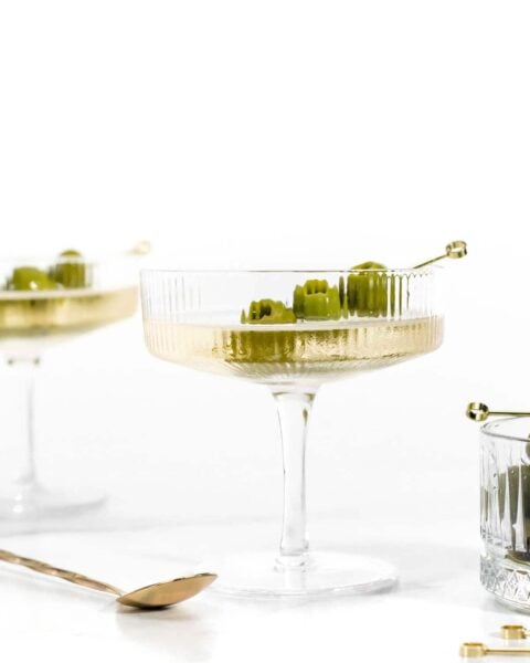 Two glasses with vodka martinis garnished with olives and a spoon.