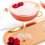Two cocktail glasses with raspberries on a tray.