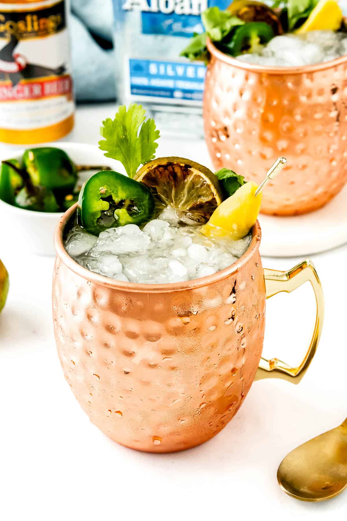 A refreshing cocktail served in a copper mug, garnished with lime, jalapeño, and a sprig of cilantro.