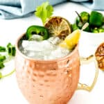 A moscow mule cocktail in a copper mug garnished with a lime wheel, jalapeño, and celery.