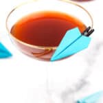 A Paper Plane cocktail recipe with blue paper airplanes in the glass.