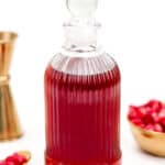 A glass bottle filled with red liquid, accompanied by pomegranate seeds and a brass container.