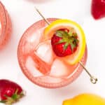 Top view of a strawberry cocktail garnished with a lemon slice and strawberry, surrounded by whole strawberries and a lemon.