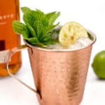 A moscow mule cocktail in a copper mug garnished with a lime wedge and fresh mint leaves.