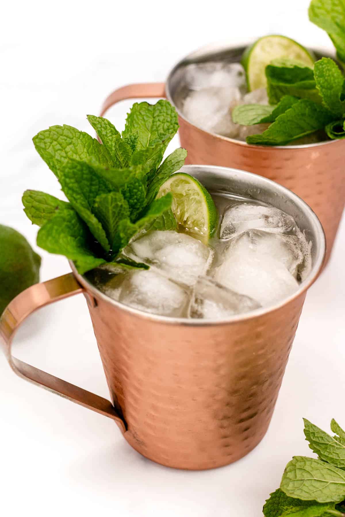 Two copper mugs filled with iced drinks garnished with lime slices and fresh mint.