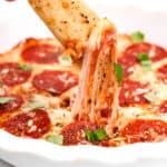 A person lifting a gooey slice of pepperoni pizza with stretchy melted cheese.