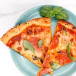 Two slices of pizza with pepperoni and basil leaves on a blue plate, with a white marble background.