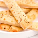 A close-up of several seasoned breadsticks stacked on a white plate.