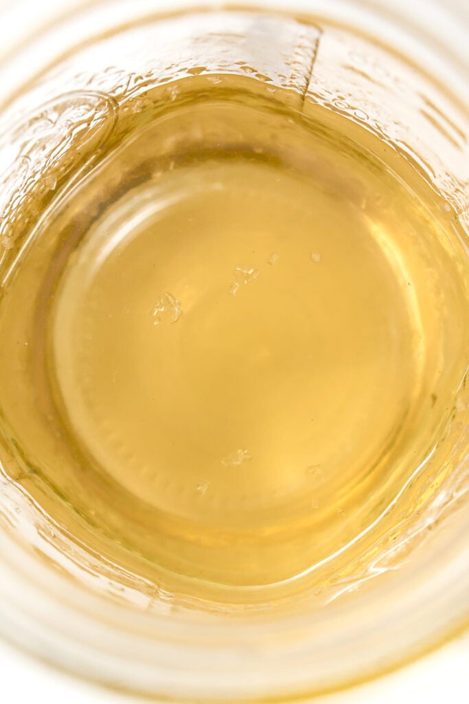 Close-up of a glass jar filled with light golden yellow simple syrup with crystallization.