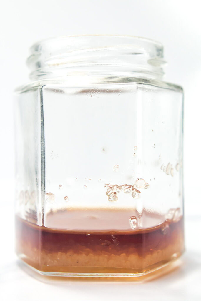 A glass jar with a small amount of brown liquid and sediment settled at the bottom.