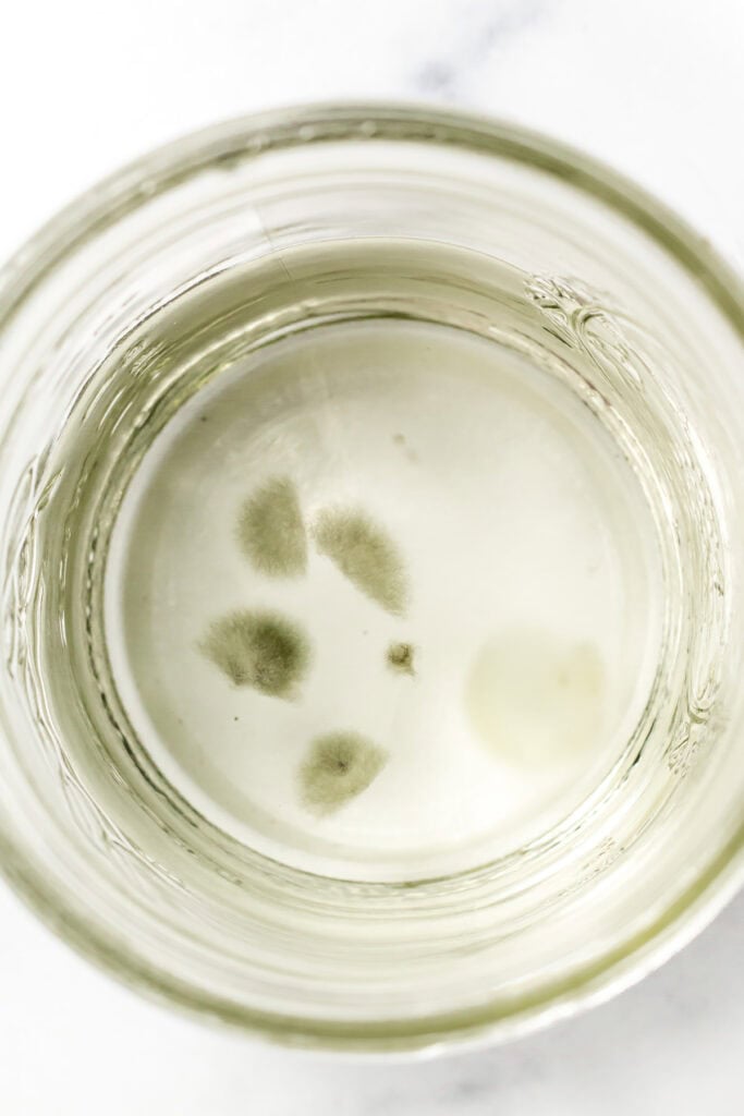 A glass jar with cloudy water and patches of mold growing on the surface, a clear sign to throw it out.
