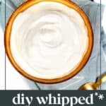 A bowl of homemade whipped cream on a light blue cloth with a spoon beside it. Text on the image reads "feast + west DIY whipped cream, easy to make homemade.