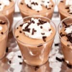 Close-up shots of several chocolate pudding mousse cups topped with whipped cream and chocolate sprinkles arranged on a metallic tray.