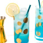 Two highball glasses with blue cocktails and ice, garnished with lemon slices and blue straws, placed on a white surface next to a gold jigger. The glasses have large gold polka dots.
