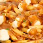Close-up of a plate of homemade poutine, showcasing golden French fries topped with cheese curds and smothered in brown gravy, garnished with a hint of herbs.