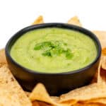 A black bowl filled with green guacamole garnished with cilantro, surrounded by tortilla chips.