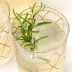 Close-up of a refreshing iced drink in a glass with a gold geometric pattern, garnished with a sprig of rosemary.