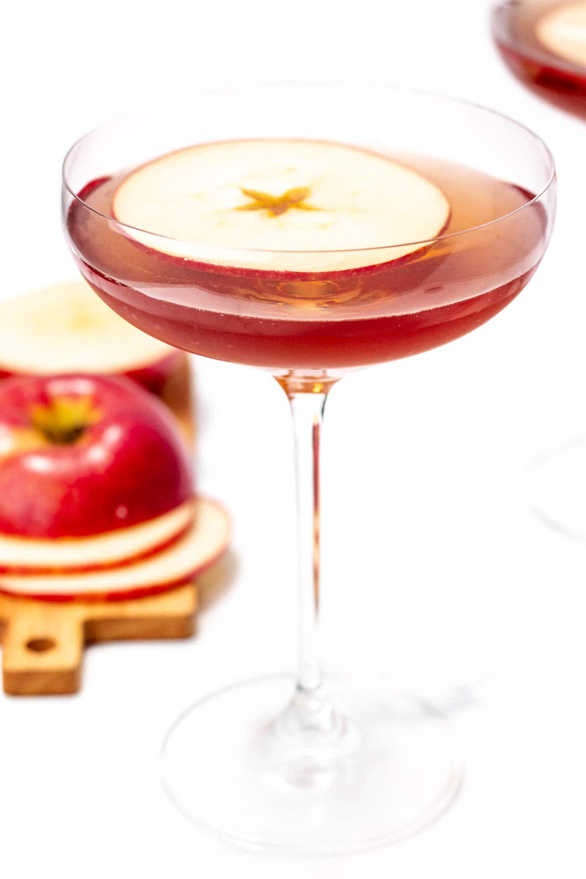 A glass of apple cider cocktail garnished with a thin apple slice.
