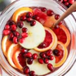A bowl of sangria with apple, orange, and blood orange slices topped with cranberries.