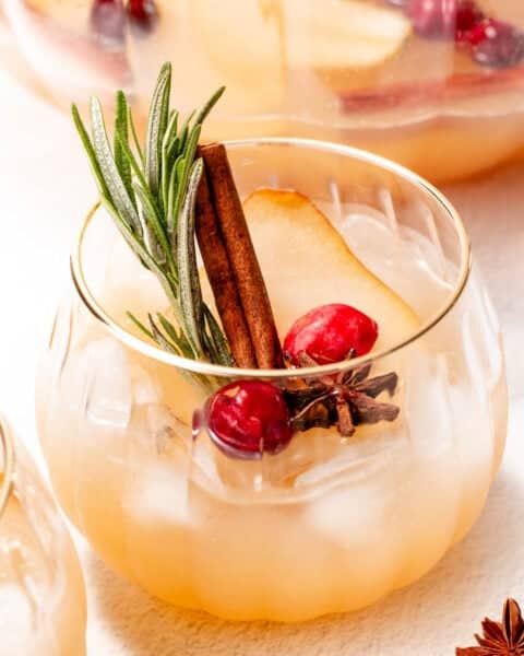 A glass of pear and cranberry infused beverage with ice, garnished with rosemary, cinnamon, and star anise.