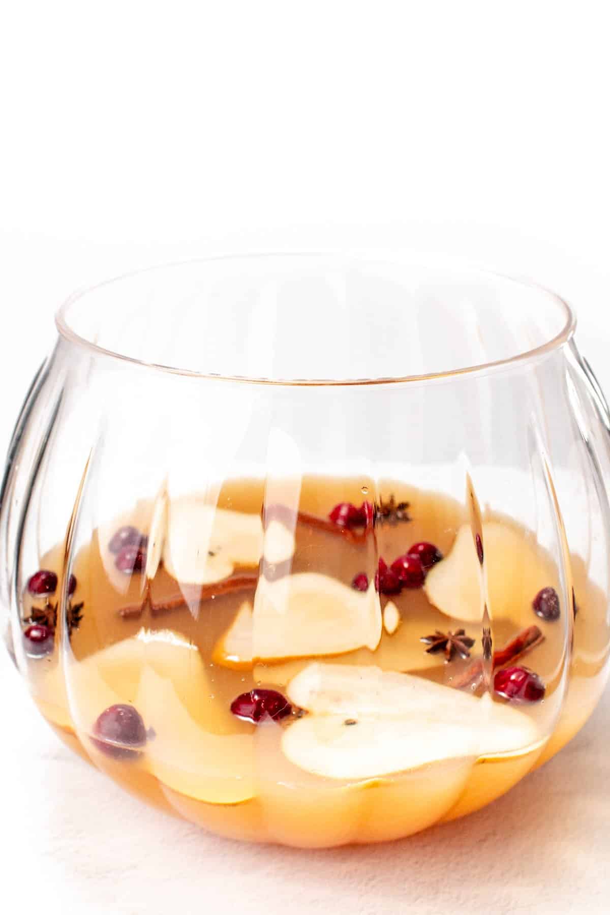 Glass punch bowl filled with orange beverage, sliced pears, and cranberries.