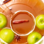 A bowl of apple cider punch with whole green apples, cinnamon sticks, and star anise floating on the surface.