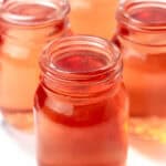 Four small glass jars filled with orange liquid are placed closely together on a white surface.