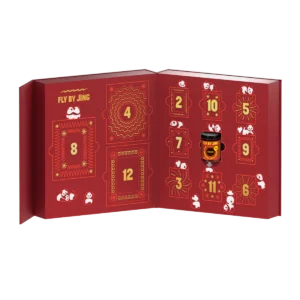 A red Fly By Jing advent calendar is opened, revealing numbered doors and a small jar of Chinese spices in slot 11. The festive design features playful panda illustrations and shimmering gold accents.