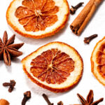 Dried orange slices, star anise, cloves, and cinnamon sticks arranged on a white surface.