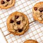 A cooling rack with six chocolate chip cookies evenly spaced on it.