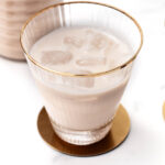 Glass of iced milk on a gold coaster, accompanied by another glass and a metallic object.