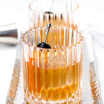 Two ribbed glasses of amber liquid with skewered cherries on a silver tray.