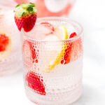 A glass of fruit-infused water with lemon slices, strawberries, and ice cubes.