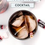 Top view of a cocktail with ice in a glass, featuring a straw. Accompanied by Tootsie Roll candies. Text reads "Easy Tootsie Roll Cocktail" and "Feast and West.