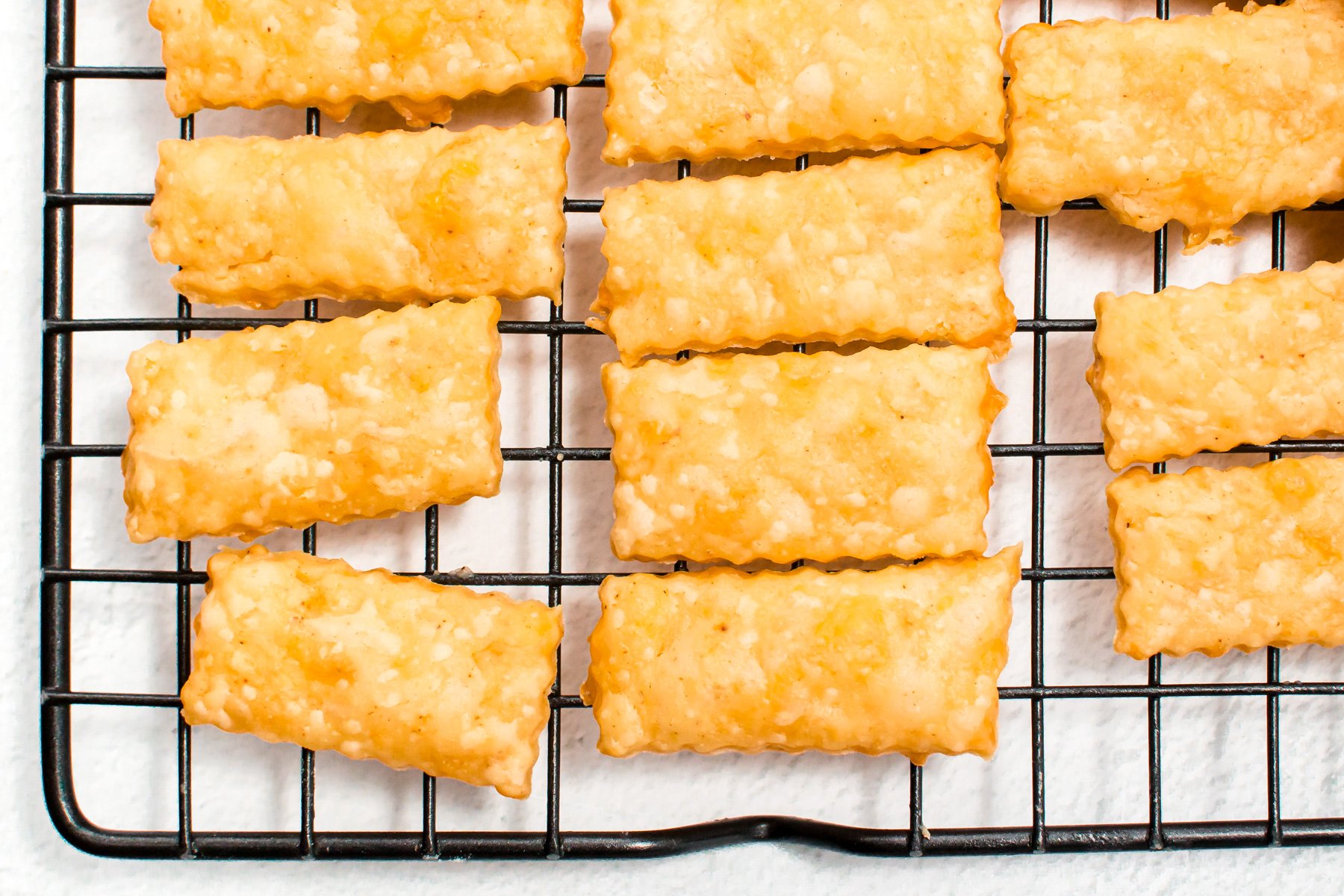 Rectangular cheese crackers with a textured surface are cooling on a black wire rack.